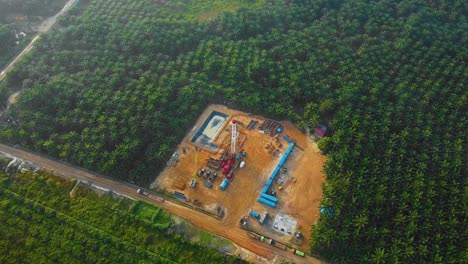 cinematic drone shot of onshore drilling and workover rig structure and rig equipment for oil exploration and exploitation in the middle of jungle surrounded by palm oil trees during sunset time