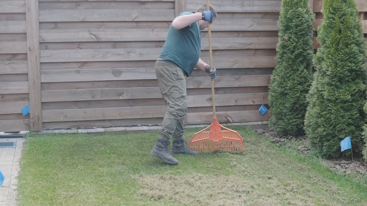 Homem Ancinhando Grama Seca e Folhas em um Jardim de Quintal