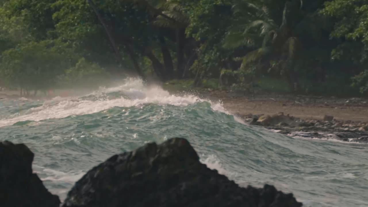 A powerful wave crashes against the rocky shoreline of Santa Teresa, sending a dramatic spray of white water into the air
