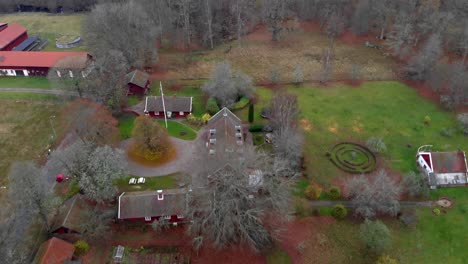 Aerial-flying-forward-over-rural-landscape,-red-traditional-farm-buildings