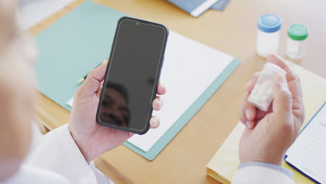 médico de edad avanzada de dos razas que usa un teléfono inteligente y sostiene medicamentos, copia el espacio en la pantalla