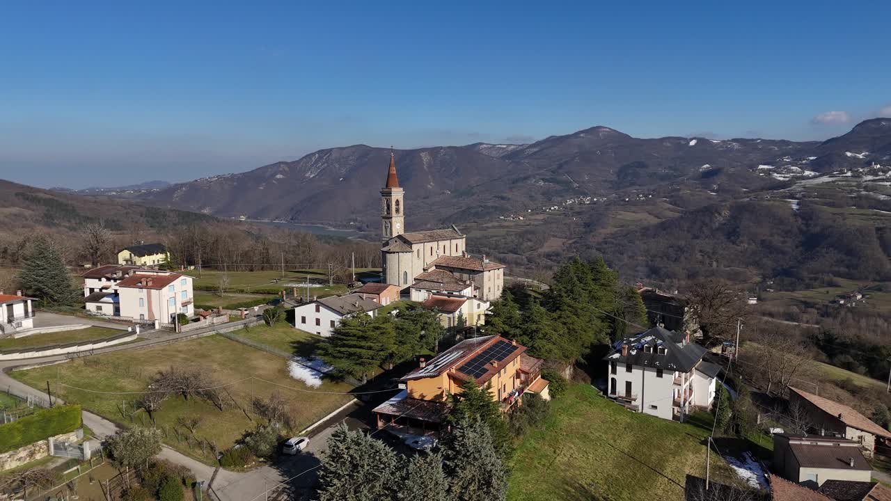 Vista aerea della storica chiesa dei Santi Salvatore e Gallo situata nel pittoresco borgo di Rabbini di Morfasso, in Italia, circondata da dolci colline e montagne