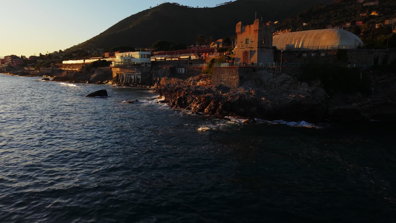 Golden hour drone shot along the Mediterranean coastline in Genoa, Italy, showing buildings