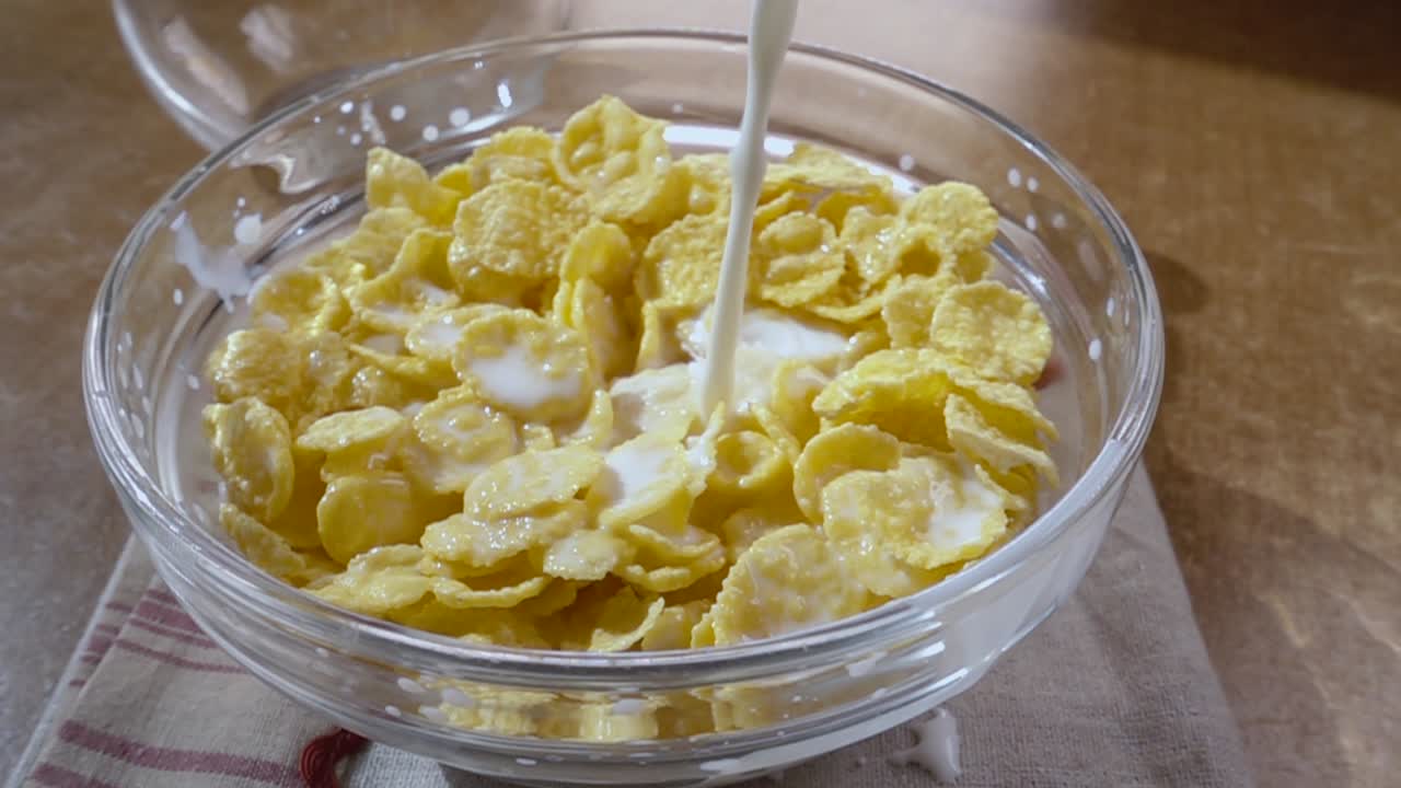 Knusprige gelbe Cornflakes in die Schale für ein köstliches Frühstück mit Milch am Morgen. Zeitlupe mit rotierender Kamerafahrt