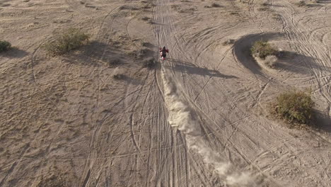 aerial: overhead dynamic shot of a dirt biker as he does a few quick skidding turns on his honda crf motorcycle in the desert and takes off into the distance