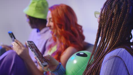 Close-Up-Studio-Shot-Of-Young-Gen-Z-Friends-Sitting-On-Sofa-Talking-And-Sharing-Social-Media-Post-On-Mobile-Phones-1