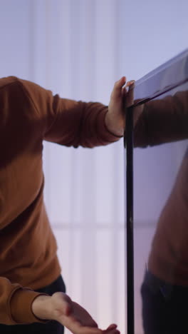 nervous long haired man slams smart tv screen standing against window light at home slow motion. guy angry of broken television device. technical problems