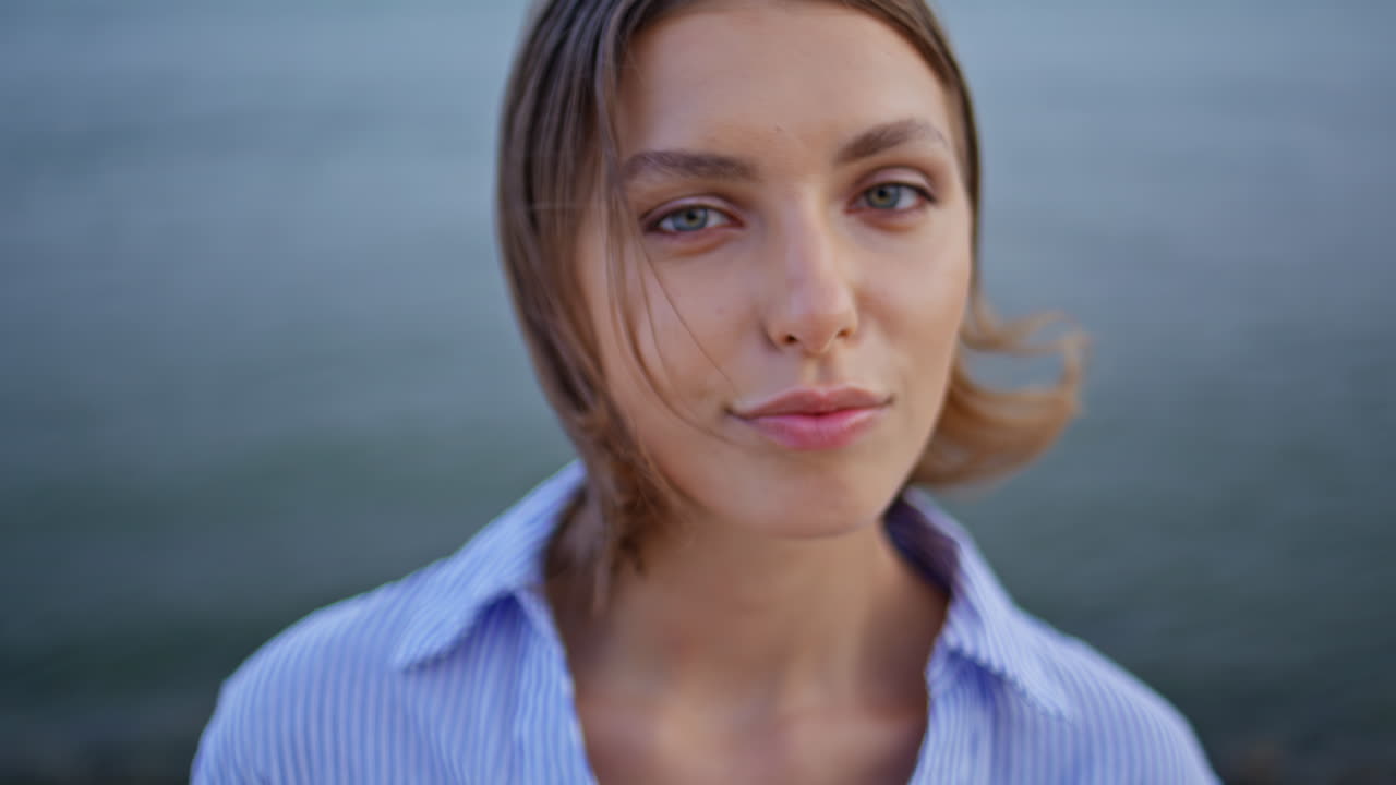 Portrait gentle girl posing by gray sea looking camera. Woman enjoy nature