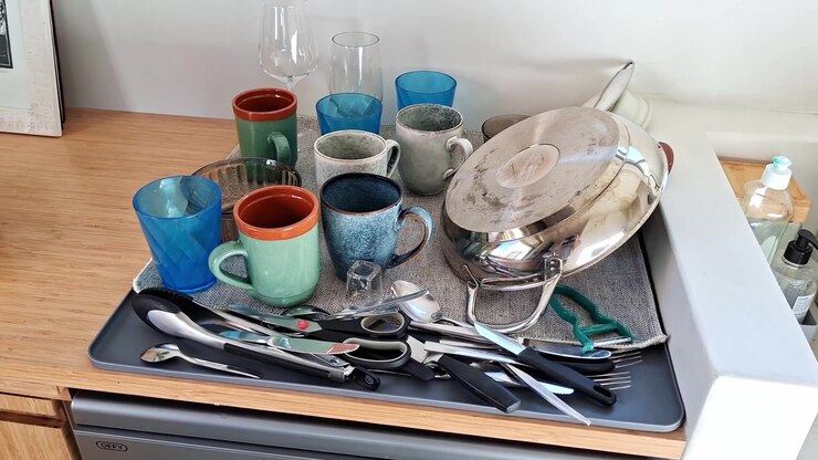 Variety of dishes, cups, glasses and cutlery drying on a drying tray in a home kitchen