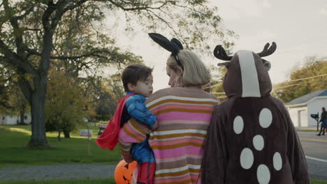 mom with two children in carnival costumes in honor of halloween. walking down the street of a small american town