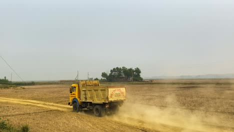 camión de construcción amarillo conduce por un camino de tierra seca en el campo de las tierras de cultivo