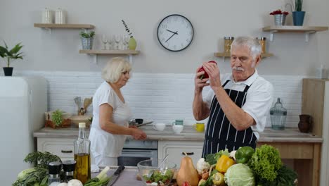 senior vegan grandmother and grandfather cooking salad with fresh vegetables in kitchen at home