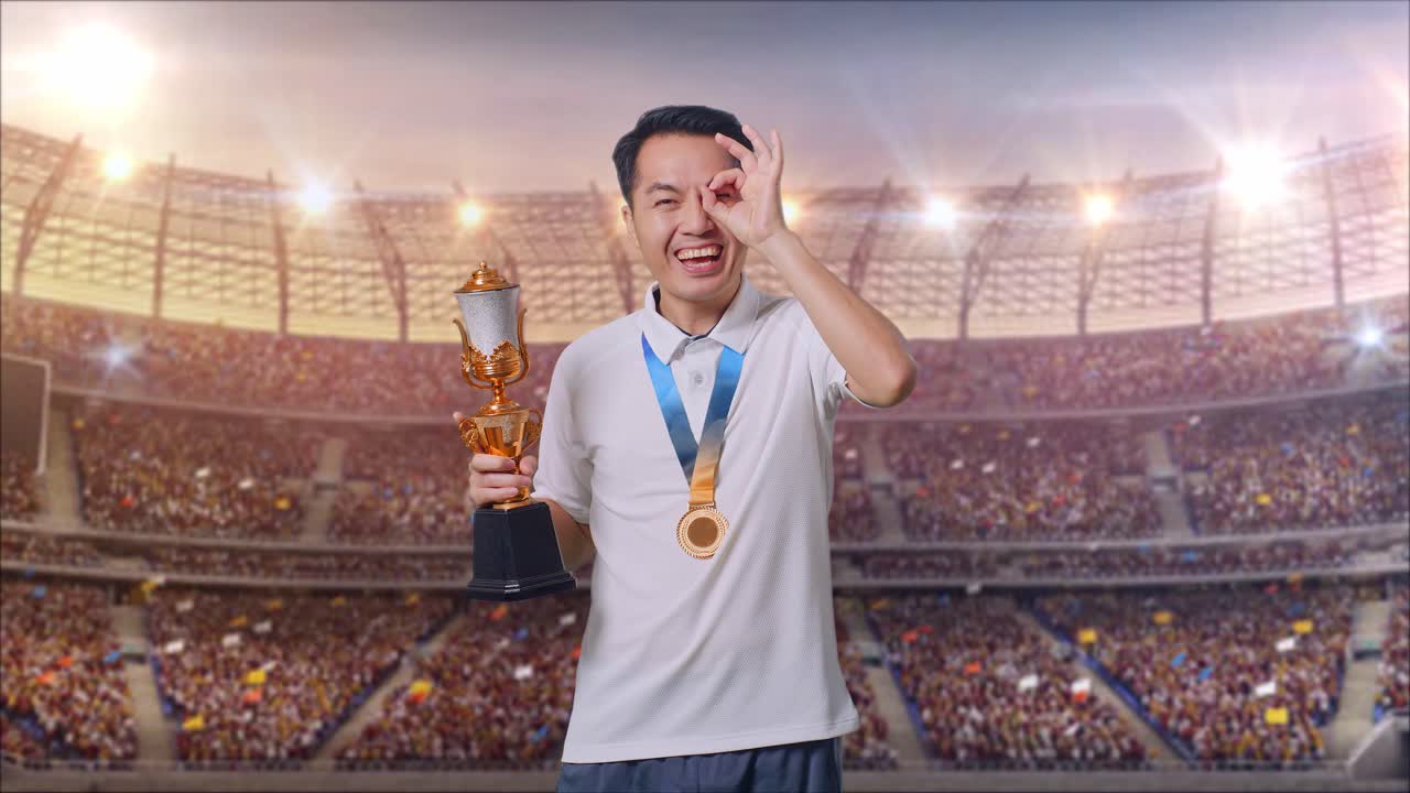 금메달과 트로피를 들고 있는 아시아인 남자가 눈 위에 손을 고 카메라를 향해 미소 짓고 있다.
