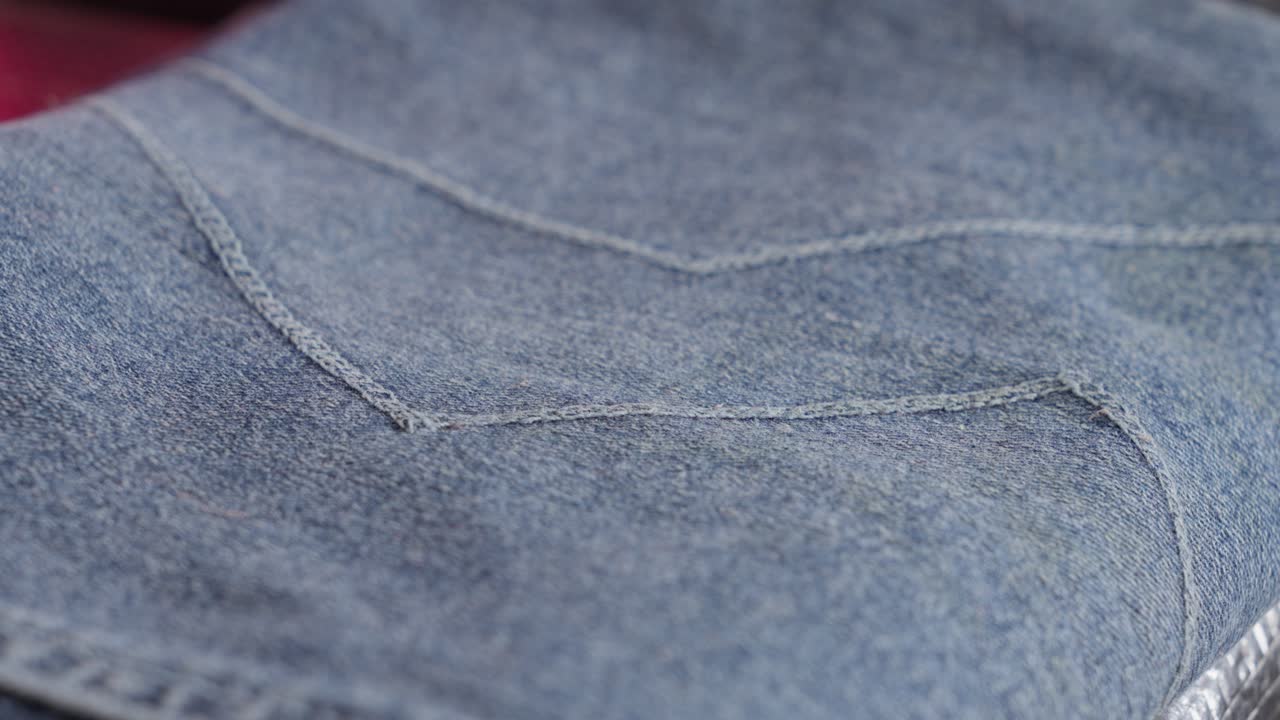 Close-up view of a person's hand touching the stitching on a pair of light blue jeans