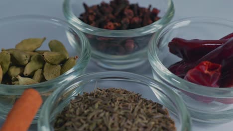 different types of whole spices cinnamon stick, black pepper, caraway seed, green cardamom, dried red chilis and cloves in small glass bowls, 4k
