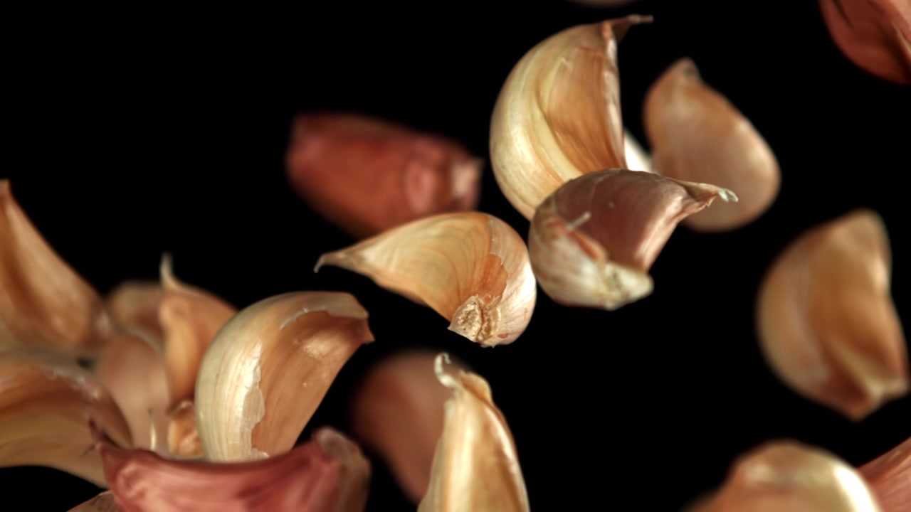 Spicchi d'aglio che cadono al rallentatore su sfondo nero
