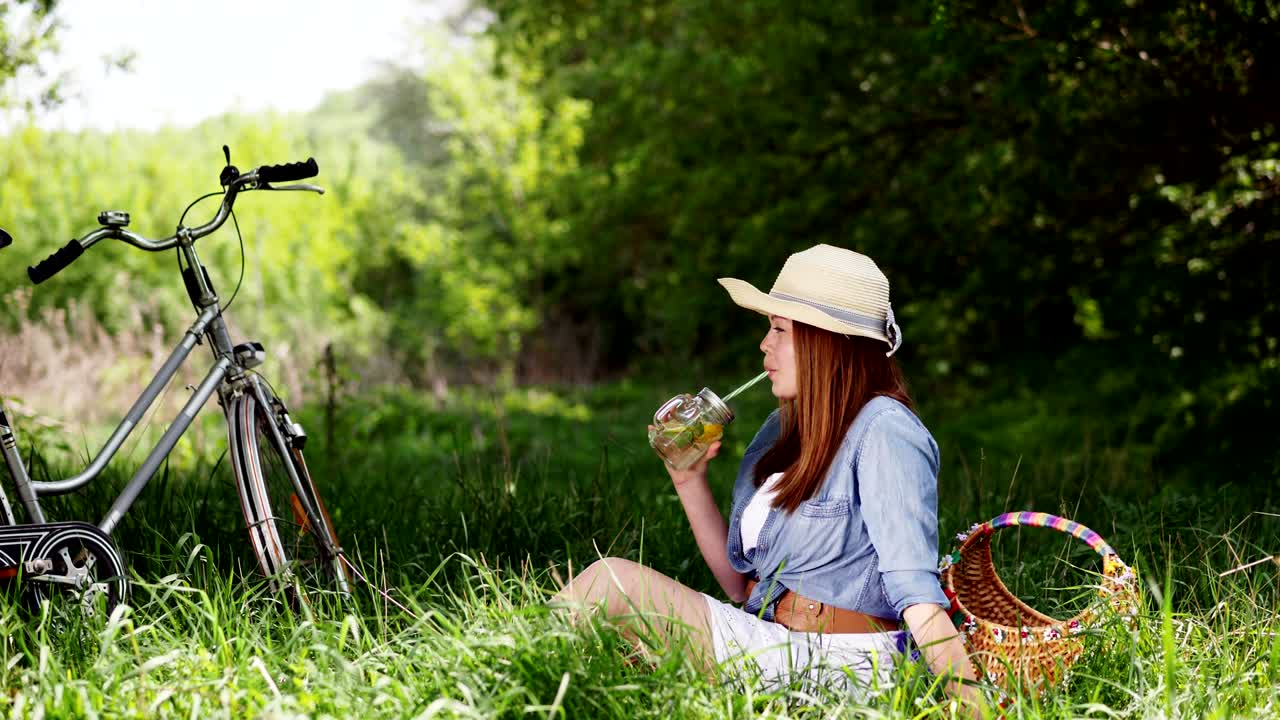 모자를 입은 미소 짓는 소녀는 자연에서 차가운 레모네이드를 즐긴다