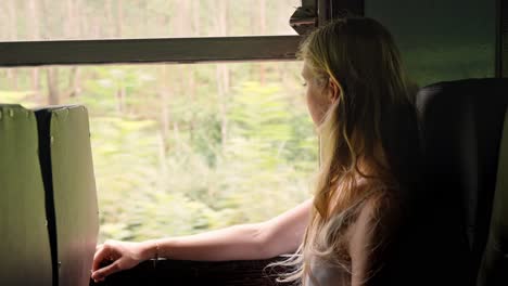 a woman sits peacefully inside a sri lankan train, gazing out the window at the lush green jungle that flanks the iconic ella to kandy railway.