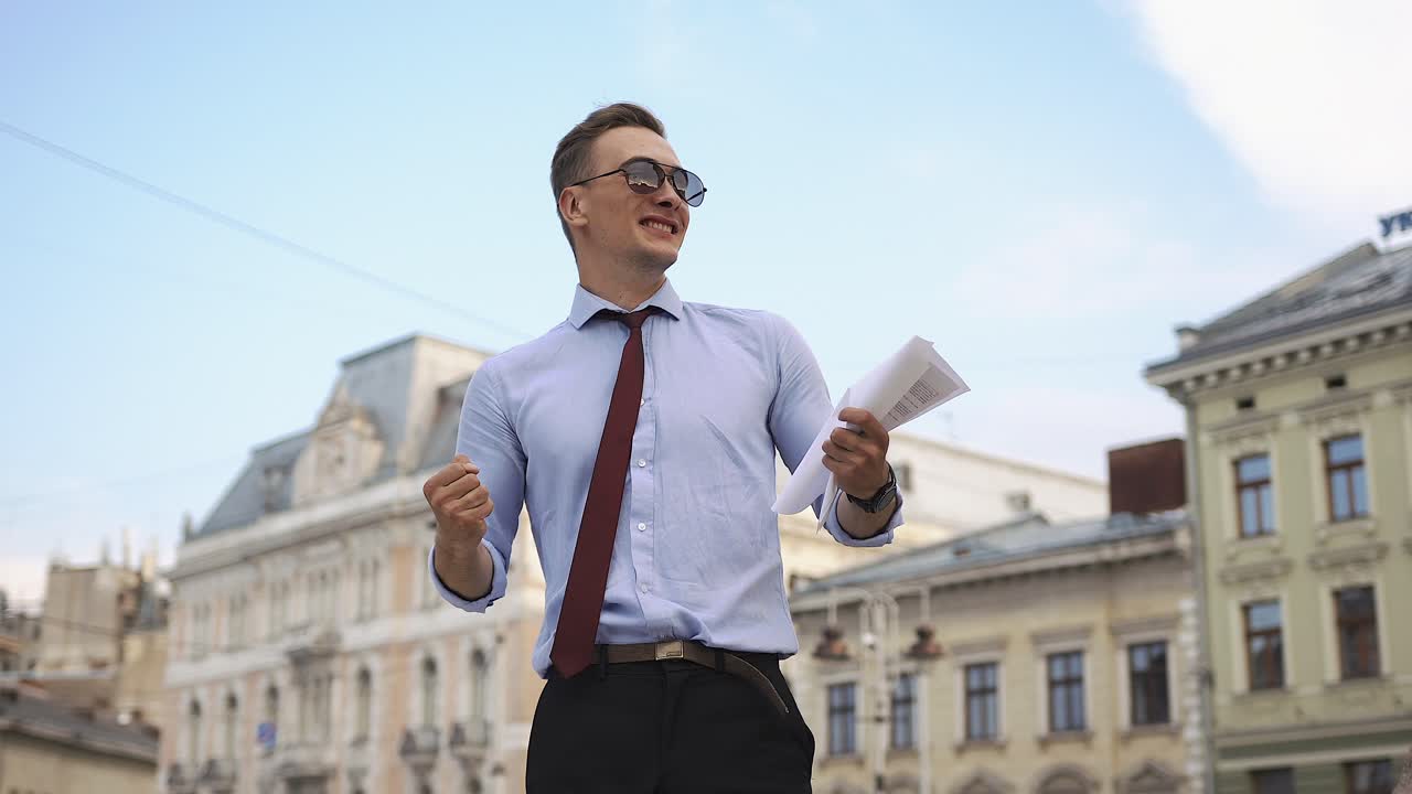 A man in sunglasses with a document outdoors in a city