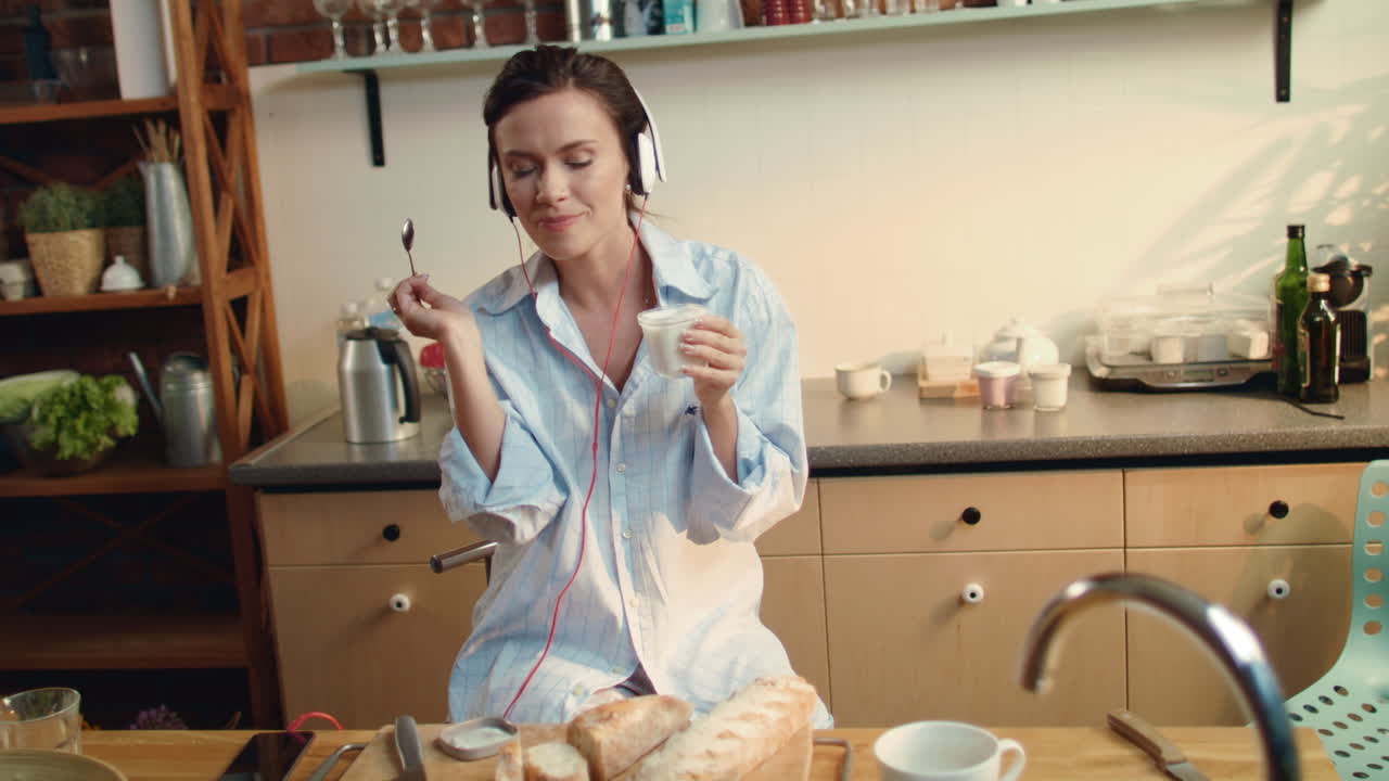 mujer comiendo yogur en la cocina. niña hermosa escuchando música con auriculares.