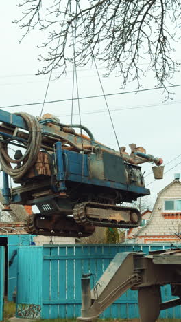 special machine for well boring hanging on the crane hook. rural village at backdrop. vertical video.