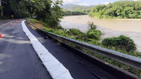 asphalt road damaged by flood along the river with high water level after heavy rain in northern thailand