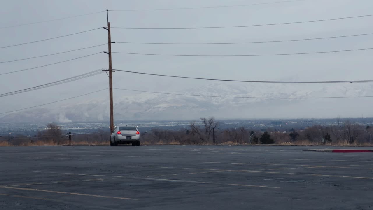 A silver car is parked and overlooking Salt Lake City, Utah from a distance with mountains far in the background on a cloudy winter day