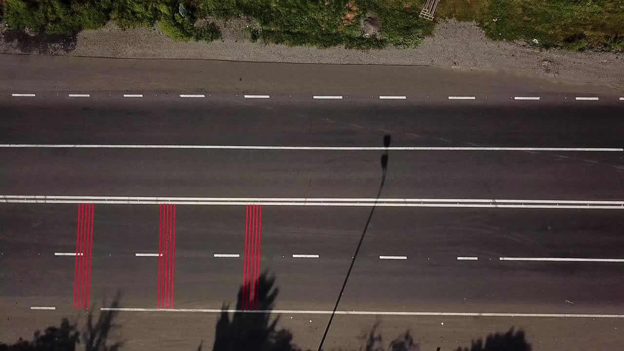 cars are passing on the road with red markings and with a pedestrian crossing. Aerial view. Camera motion to right
