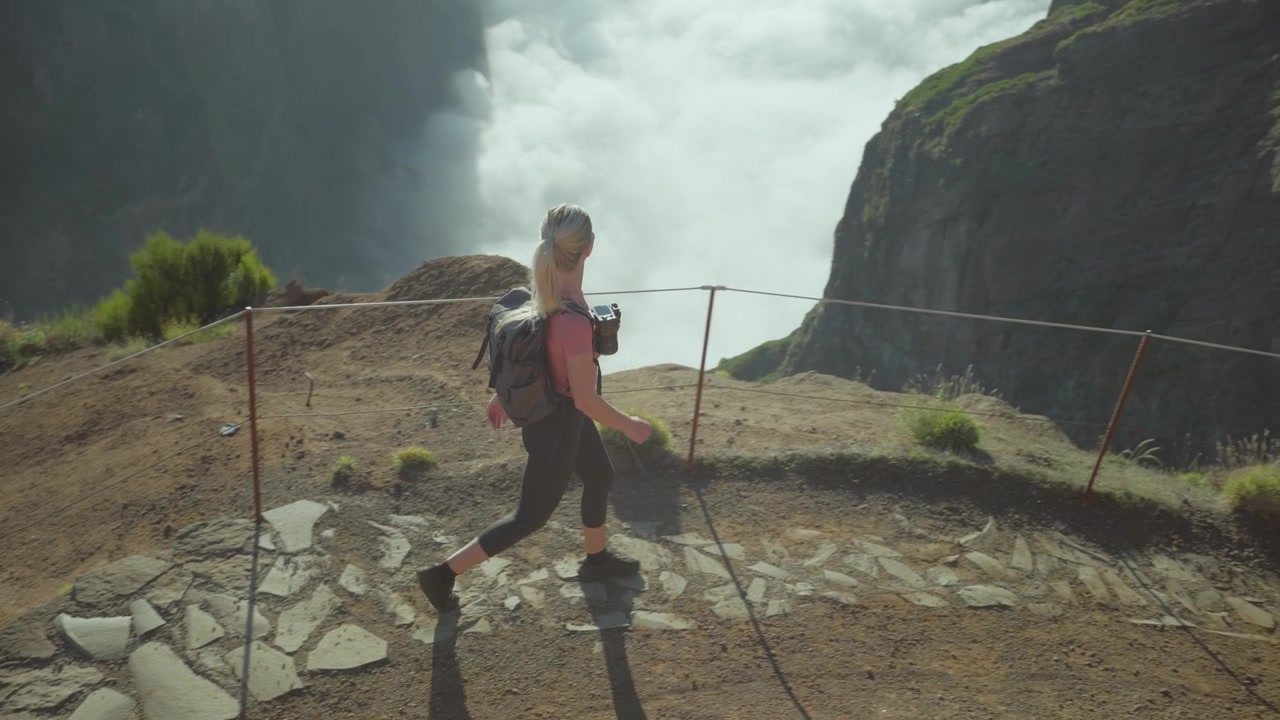 Blond female hiker with backpack walking on mountain trail during golden hour