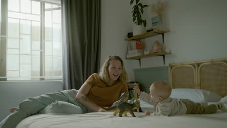 mother and baby playing with dinosaurs on a bed