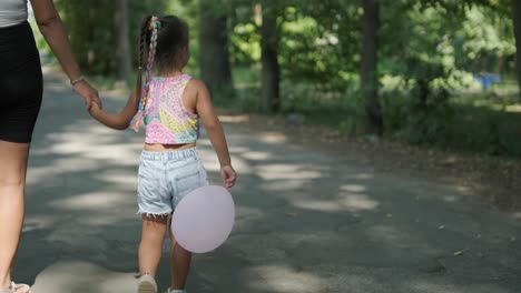 pregnant mother and daughter walking in park with balloon