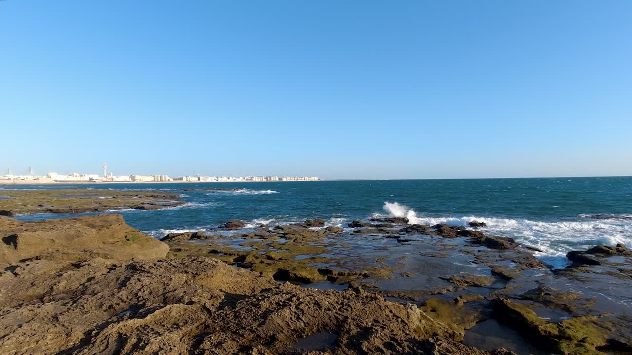 olas rompiendo a cámara lenta en una playa rocosa en un día de cielo azul claro