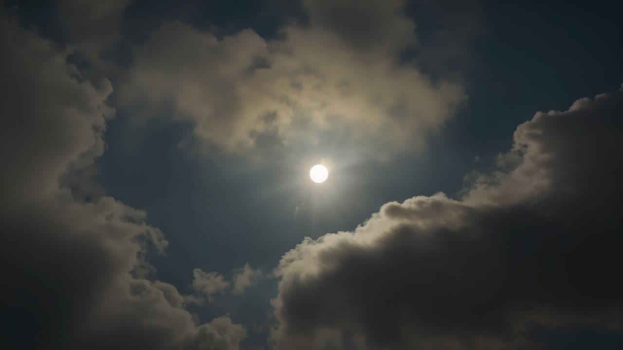 Wind driving cumulus clouds drifting right then parting revealing sun disc shining in daytime sky