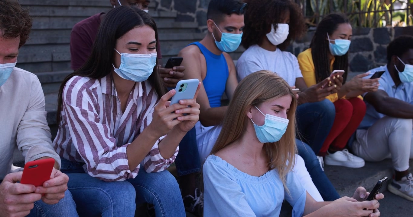 Jóvenes diversos con mascarillas usando smartphones al aire libre