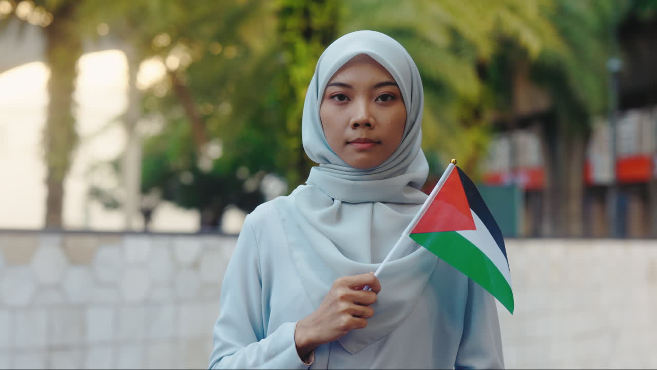 Young Muslim Woman in Hijab Holding Palestinian Flag Outdoors