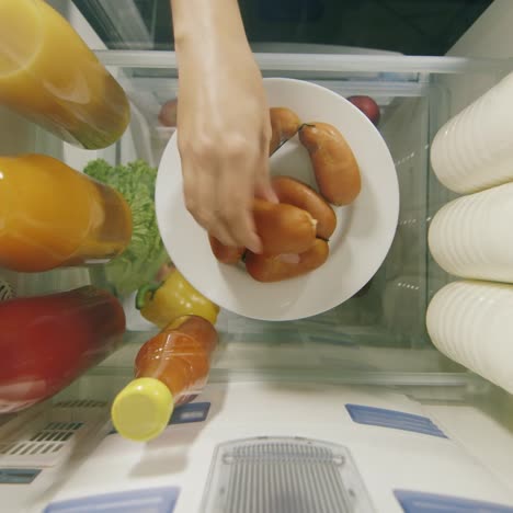 midnight snack view from inside the refrigerator - women's hands take sweets from a plate 1