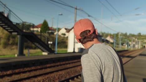 young man wearing hat and standing on railway platform watching for train coming