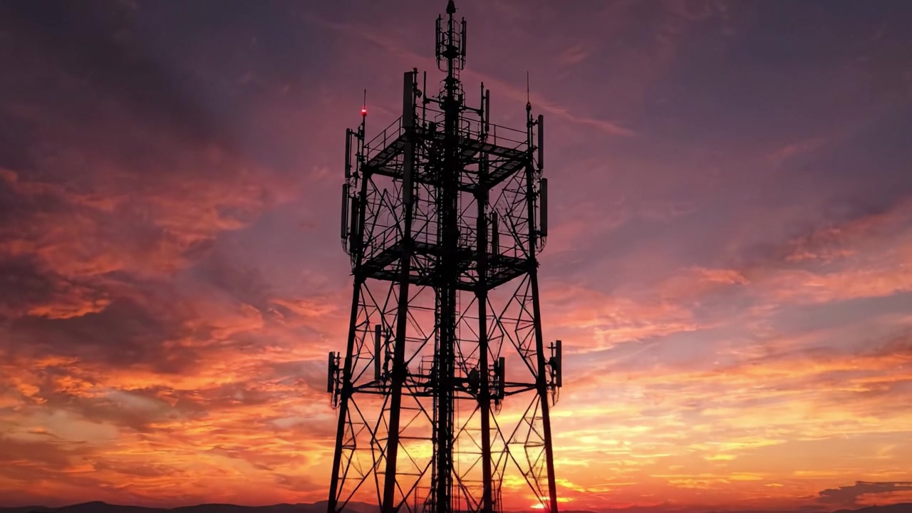En transcendent solnedgang: Et elegant kommunikationstårn i silhuet mod en fantastisk himmel fyldt med levende farver og dramatiske skyformationer.