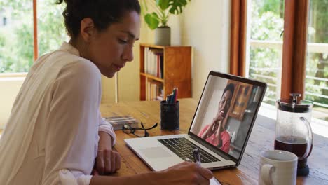 african american woman taking notes while having a video call on laptop at home