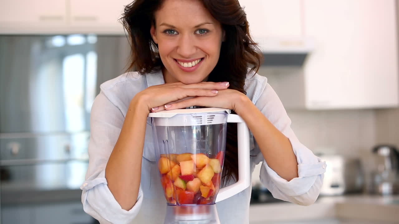 Bella brunetta appoggiata al frullatore che sorride alla fotocamera.