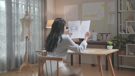 화가 난 아시아 여성 가방 디자이너의 뒷면은 사무실에서 레이아웃을 보면서 머리를 긍정적으로 흔들고 있습니다.