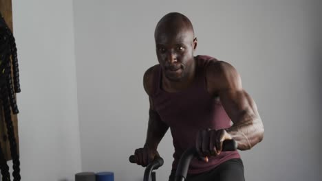 hombre afroamericano en forma haciendo ejercicio en bicicleta de entrenamiento dentro del gimnasio