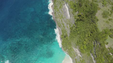 Top-Drohnenaufnahme-Des-Strandes-Von-Nusa-Penida-Auf-Bali,-Die-Das-Ende-Des-Sandstrandes-Und-Die-üppig-Grünen-Klippen-Der-Küste-Einfängt,-Wobei-Das-Türkisfarbene-Wasser-Eine-Atemberaubende-Und-Ruhige-Aussicht-Bietet