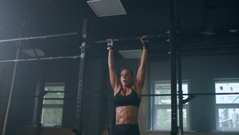 female athlete swinging on chin up bar. strong women doing chin-ups on gymnastic bars in gym. professional athlete does chin-up power strength and cross fitness exercises and everyday workout routine.