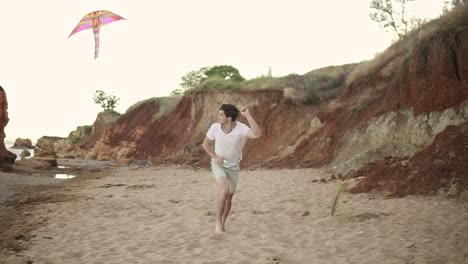 young attractive man releasing colorful kite against a blue sky on the beach in the evening. slow motion shot