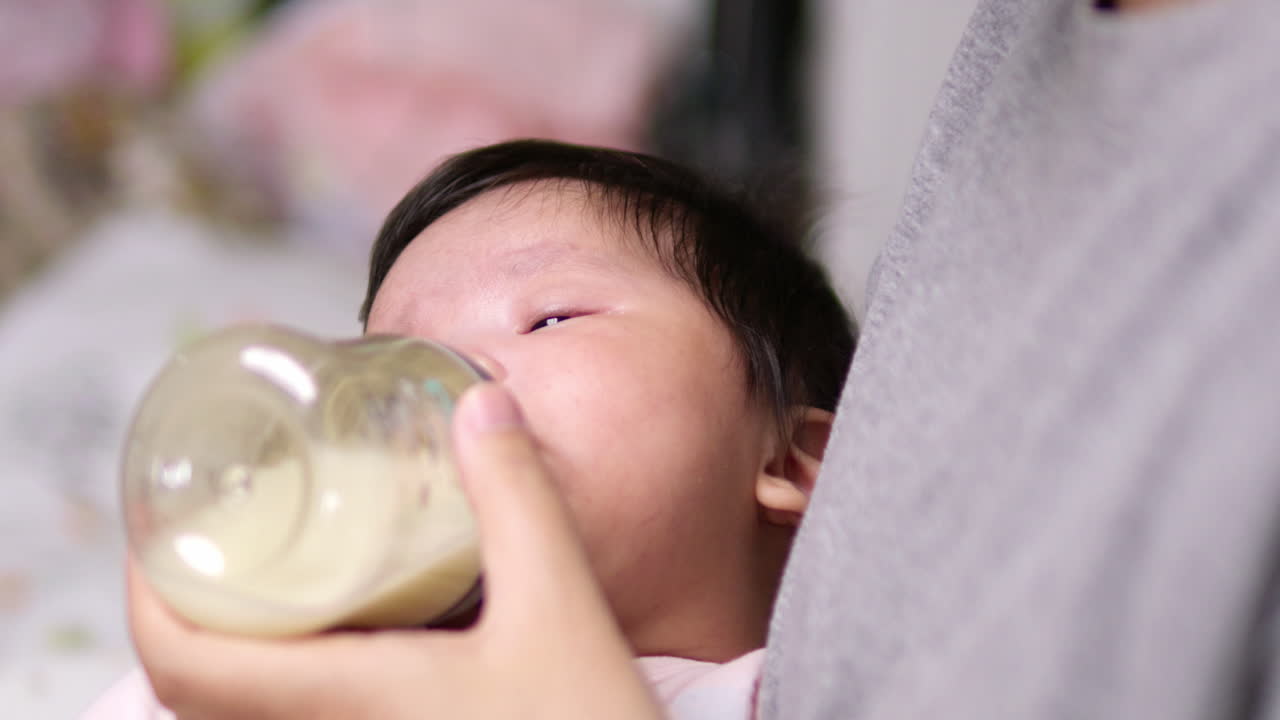 Panning from a blurry to a clear shot of a baby who is drinking some milk as she is cradled in her mother's arms.