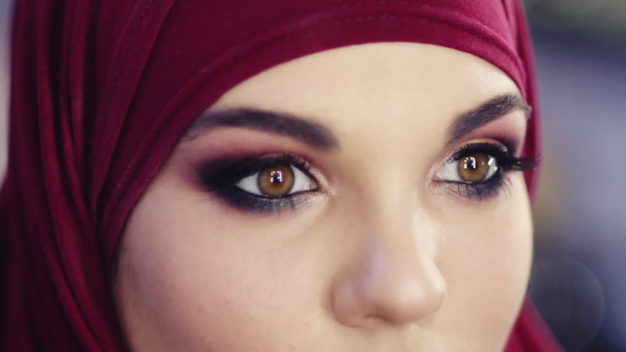 히자브를 입은 소녀가 완벽한 다채로운 스모키 메이크업으로 눈을 뜨는 느린 움직임의 클로즈업 영상