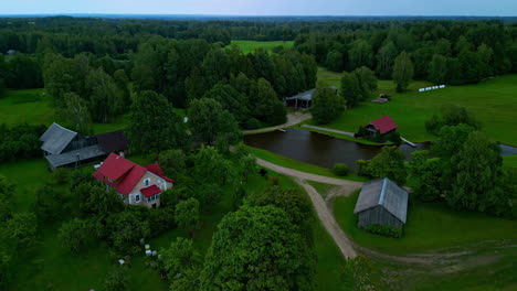 Eine-Ruhige-Ländliche-Landschaft-Mit-Einem-Teich,-Grünen-Feldern-Und-Einem-Haus-Mit-Rotem-Dach-In-Der-Abenddämmerung-Aus-Der-Vogelperspektive