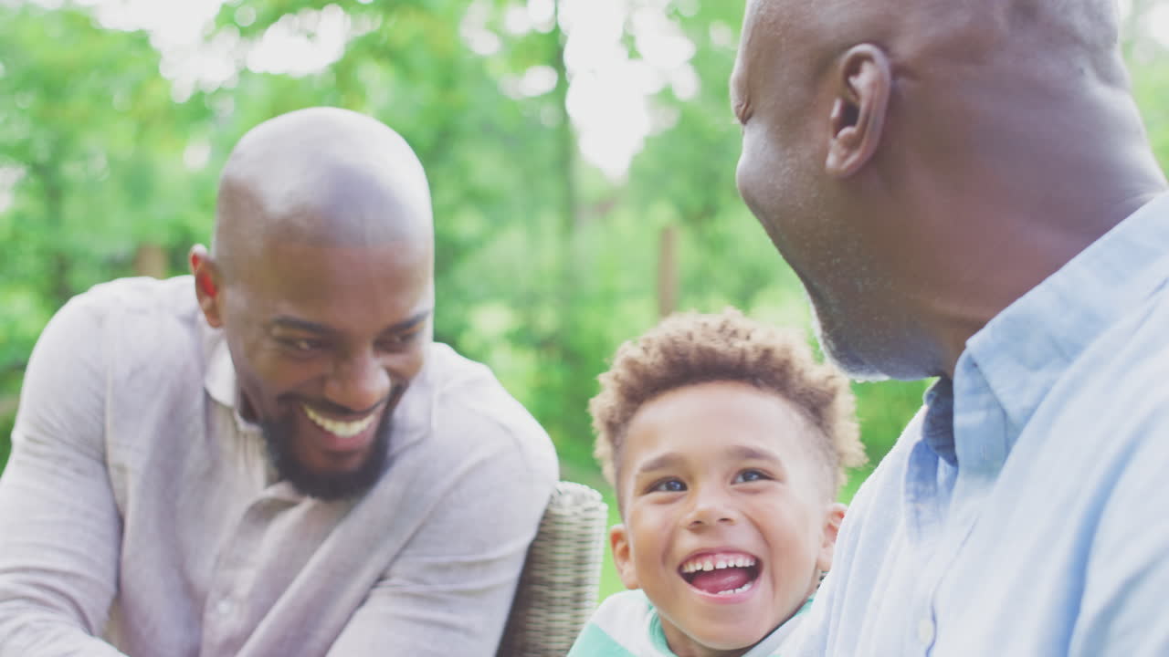 Smilende mandlig familie med flere generationer derhjemme i haven sammen.
