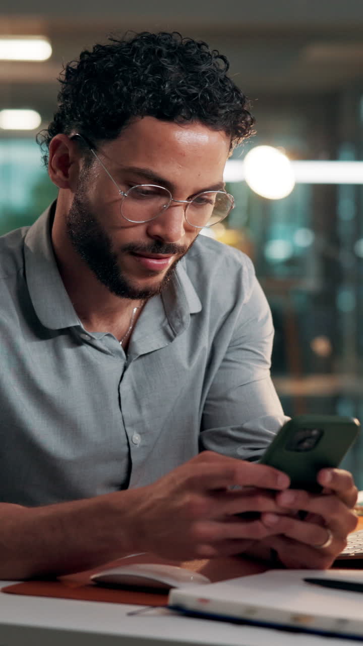 Young Man with Glasses Using Smartphone at Desk in Office